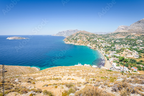 Beautiful sunny coast view to the greek blue sea with crystal clear water beach with some boats fishing cruising surrounded by hills mountains, Kantouni, Patmos, Kos, Dodecanese Islands, Greece 