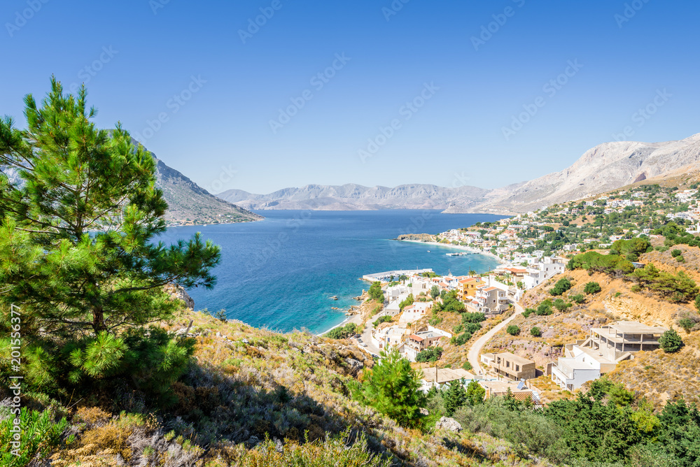 Beautiful sunny holiday view to the greek beach blue sea with crystal clear water beach with some boats fishing cruising surrounded by hills mountains, Kalymnos Island, Kos, Dodecanese, Greece 