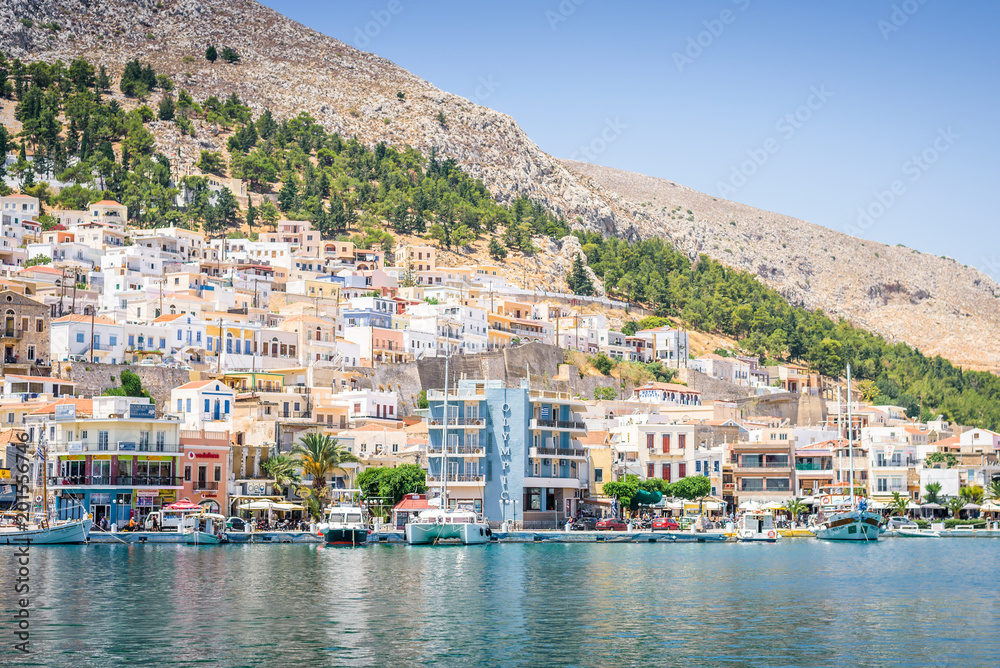 Beautiful sunny coast view to the greek blue sea with crystal clear water to the traditional town of Pothia surrounded by hills mountains with boats in harbor, Kalymnos Island, Kos, Dodecanese Greece