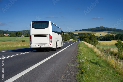Obraz na płótnie White bus traveling on asphalt road in a rural landscape with village and mountain in the background w salonie