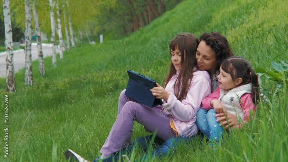 Family with a tablet on the nature. Children with mom in the park with a gadget. Family with a tablet on the nature. Children with mom in the park with a gadget.