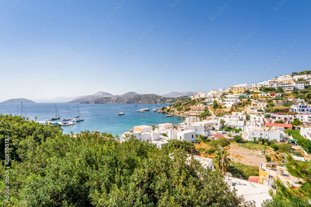 Beautiful sunny greek village town harbor view to the aegean blue sea with crystal clear water boats cruising surrounded by hills mountains windmills on top, Panteli, Leros, Dodecanese Islands, Greece
