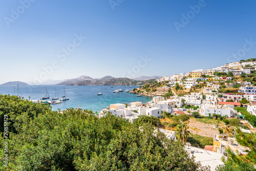 Beautiful sunny greek village town harbor view to the aegean blue sea with crystal clear water boats cruising surrounded by hills mountains windmills on top, Panteli, Leros, Dodecanese Islands, Greece