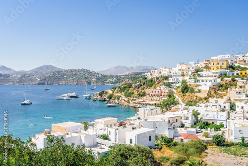 Beautiful sunny greek village town harbor view to the aegean blue sea with crystal clear water boats cruising surrounded by hills mountains windmills on top, Panteli, Leros, Dodecanese Islands, Greece © Thomas Jastram