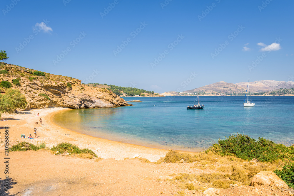 Beautiful sunny coast view to the greek blue sea with crystal clear water beach with some boats fishing cruising surrounded by hills, Kokkina Beach, Leros, Dodecanese Islands/ Greece – July 18 2017