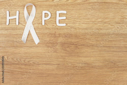 Oncological disease concept. Word "hope" written with a white ribbon as a symbol of lung cancer on wooden background