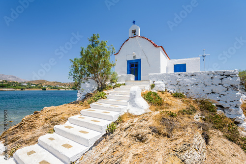 Holy white and blue chruch of agios Isidoros shining at an empty place in the greek sea only reachable by a stone boardwalk over the water on the island of Leros, Dodecanese, Greece photo