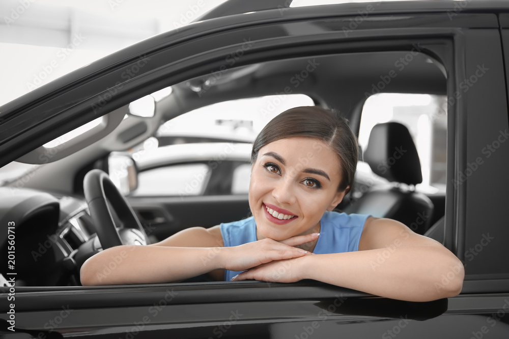 Young woman sitting in driver's seat of new car at salon