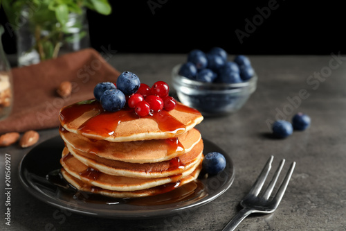 Stack of tasty pancakes with berries and syrup on table