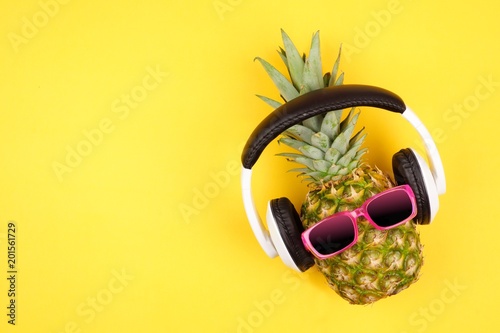 Hipster pineapple with sunglasses and headphones. Top view against a yellow background. Minimal summer concept.