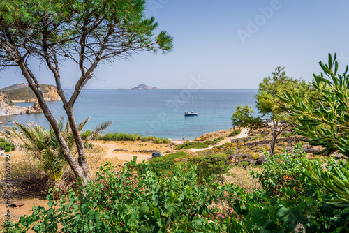 Peaceful sunny coast view to a empty greek holiday bay with crystal clear blue water sandy beach for sunbathing and some boats cruising fishing in background