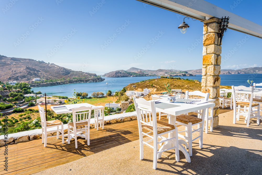 Your table is already reserved at the greek mediterranean sea behind crystal clear blue water and a beautiful coastal aegean bay with fishermen boats cruising, Patmos Island, Kos, Dodecanese, Greece