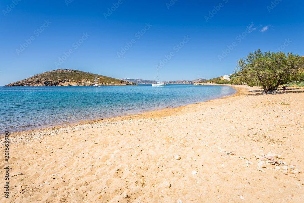 Amazing sunny coast view to a empty holiday bay Didymes beach with crystal clear blue water sandy beach for sunbathing and some boats cruising fishing in background, Patmos Island, Dodecanese, Greece