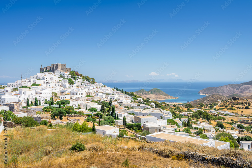 Amazing sunny view from old monastery castle Chora a small greek town near Skala with harbour and blue sea with crystal clear water surrounded by hills mountains, Patmos Island, Dodecanese, Greece