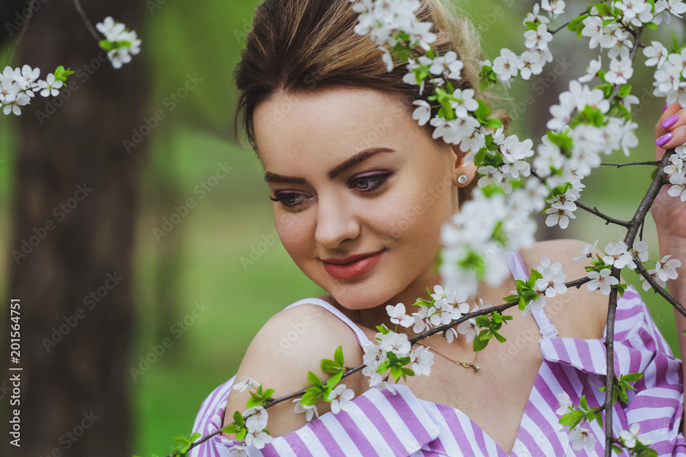 Fototapeta premium Beautiful blonde girl with blond hair in a dress on a background of spring blooming trees