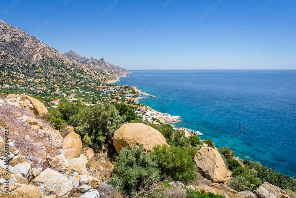 Beautiful sunny greek village town church and harbor view to the blue sea with crystal clear water and fishing boats cruising yacht at shore, Ikaria Island, Karkinagri, Sporades/ Greece – 08 01 2017