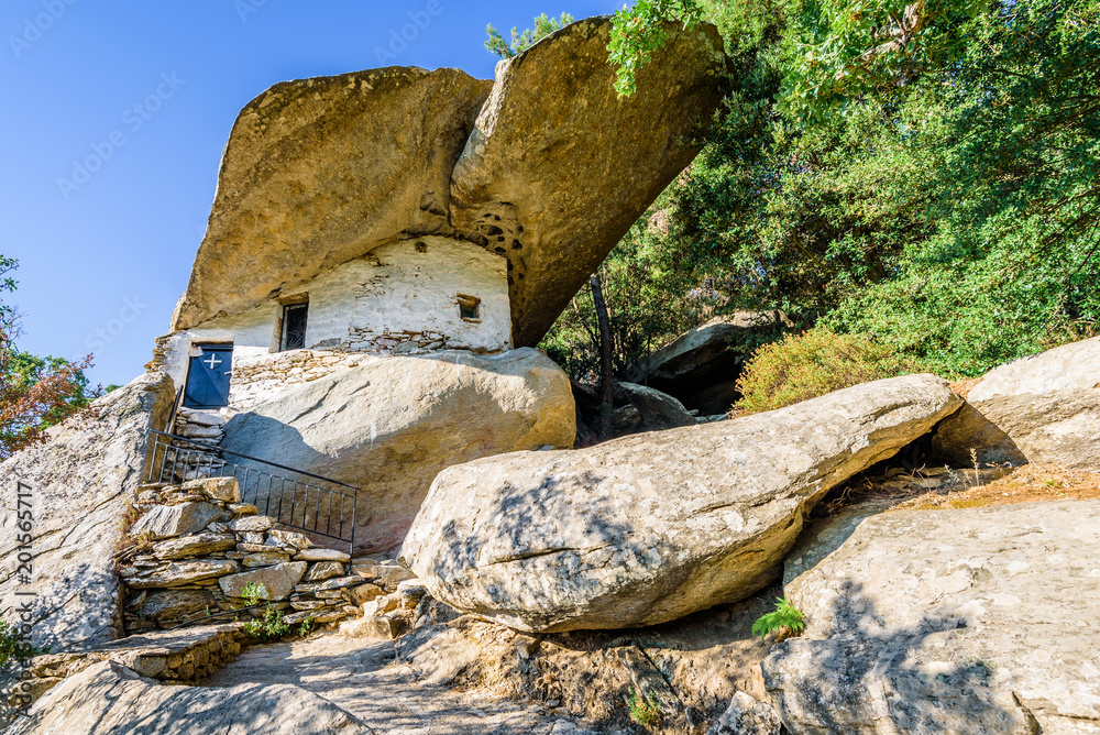 Holy old ancient greek white stone Monastery church called Theoktistis shining over island at the mediterranean sea sourrounded by beautiful landscape and hidden by rocks in moutains, Ikaria, Greece