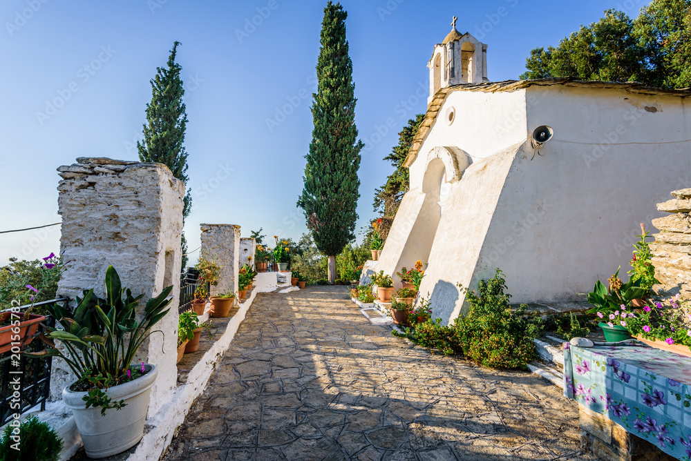 Holy old ancient greek white stone Monastery church called Theoktistis shining over island at the mediterranean sea sourrounded by beautiful landscape and hidden by rocks in moutains, Ikaria, Greece