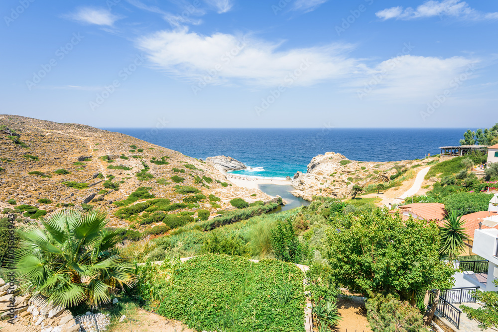 Beautiful sunny summer coast view to the greek blue sea with crystal clear water sandy holiday relaxing beach with some boats fishing cruising surrounded by hills mountains, Ikaria, Sporades, Greece 
