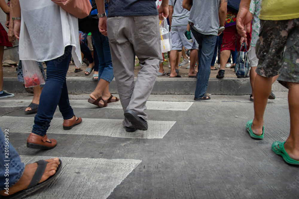 People walk across the street across the crosswalk. Selective focus on feet of people. People walk across the street across the crosswalk. Selective focus on feet of people.