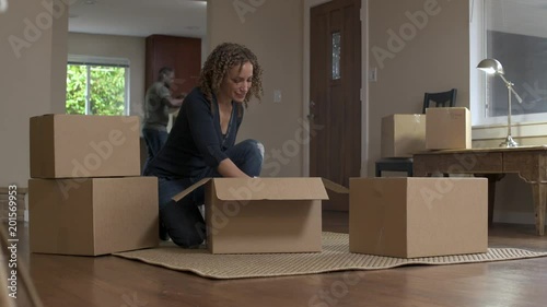 Woman crouching on floor, unpacking crockery from boxes, looking at camera, smiling.  photo