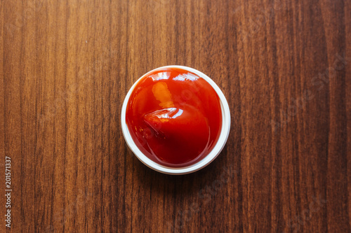 A cup of ketchup place on wooden table.