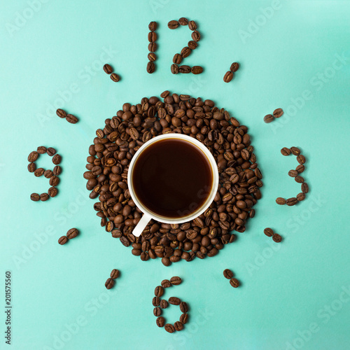 Coffee cup and roasted beans arranged as clock face on blue background, top view. Coffee time symbol. Interesting idea energy and refreshment concept. photo