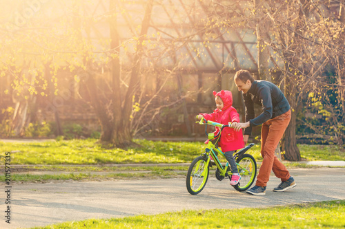 Happy father teaching his little daughter to ride a bicycle. Child learning to ride a bike. Family activities at summer