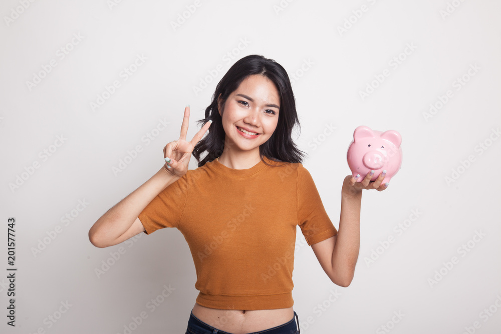 Asian woman show victory sign with pig coin bank. Asian woman show victory sign with pig coin bank.