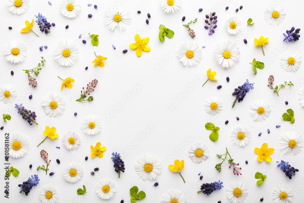 Floral frame made of colorful spring flowers and green leaves on white background. Flat lay, top view.