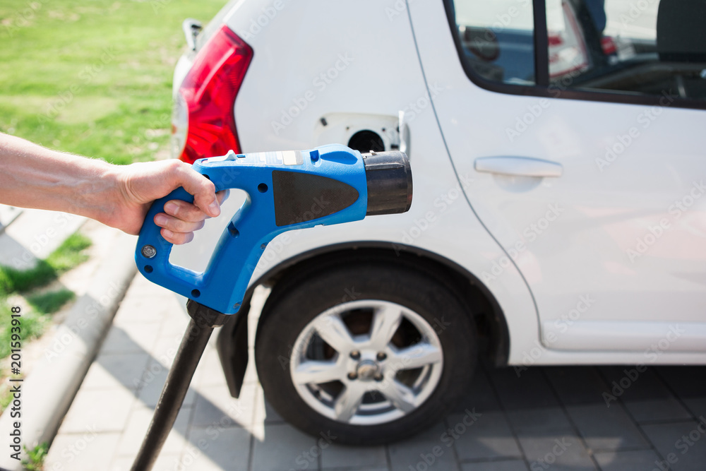 A man holds a charger plug for an electric car. A man holds a charger plug for an electric car.