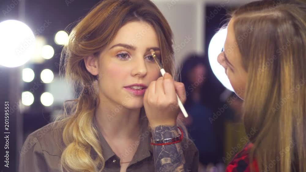 Portrait. Young attractive woman in visage studio. Professional makeup artist correcting the shape of eyebrow with special brush. Reflection in the mirror Portrait. Young attractive woman in visage studio. Professional makeup artist correcting the shape of eyebrow with special brush. Reflection in the mirror