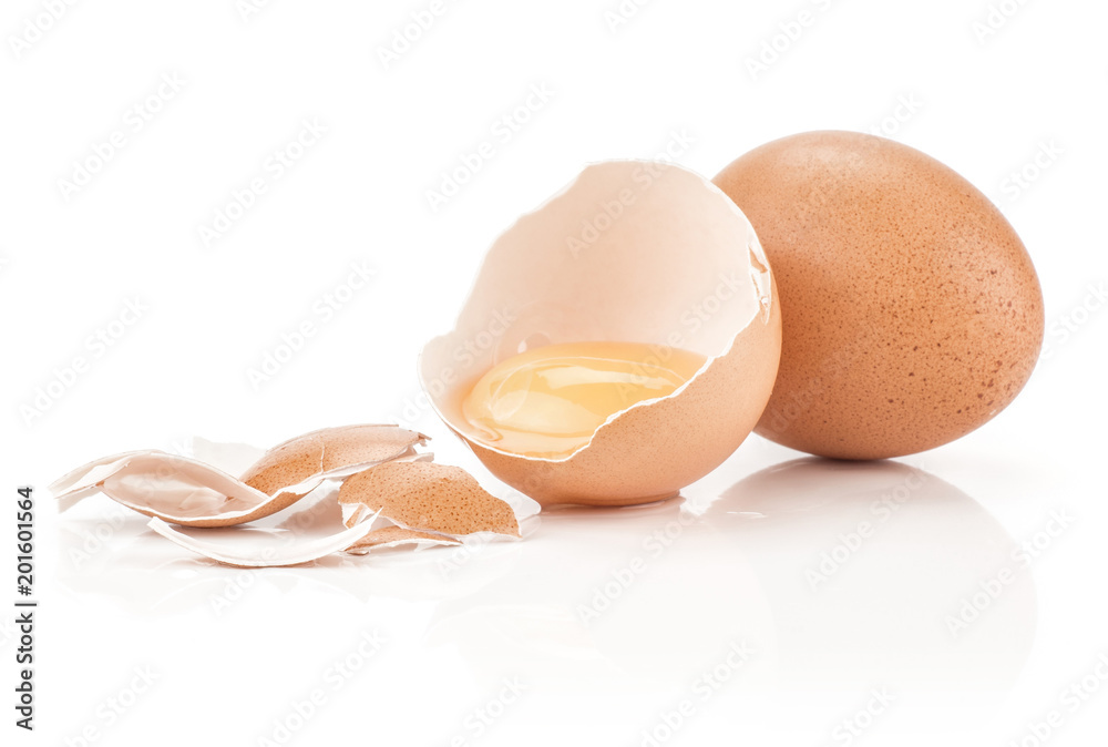 One raw yolk in a brown chicken eggshell half with a lot of cracked pieces and one whole egg isolated on white background. One raw yolk in a brown chicken eggshell half with a lot of cracked pieces and one whole egg isolated on white background.