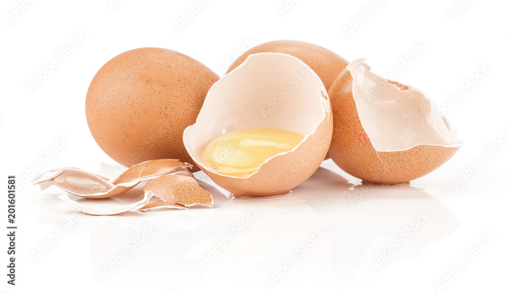 Two brown chicken eggs and one raw yolk in an eggshell half with a lot of cracked pieces isolated on white background. Two brown chicken eggs and one raw yolk in an eggshell half with a lot of cracked pieces isolated on white background.