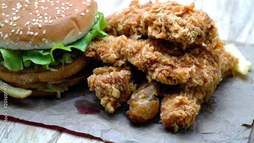 Crispy fried chicken wings and legs, cheeseburger with french fries on a wooden table rotation. Breaded Crispy chicken, fried potato, cheeseburger tasty dinner. Crispy fried chicken wings and legs, cheeseburger with french fries on a wooden table rotation. Breaded Crispy chicken, fried potato, cheeseburger tasty dinner.