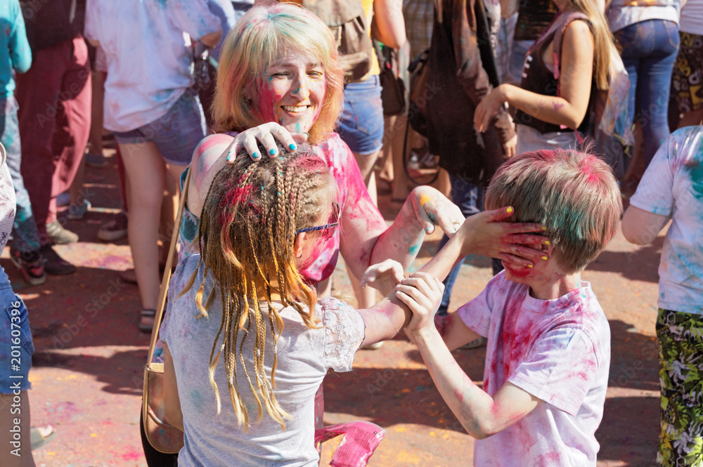 Cheerful mother and her children smear dry paint on each other's body and clothes
