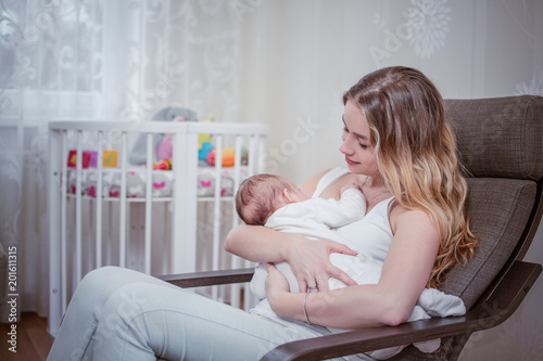 Obraz na płótnie Breastfeeding baby near crib. Pretty mother holding her newborn child. Mom nursing baby. Beautiful woman and new born relax at home in nursery interior. Blondе mother breast feeding baby. w salonie