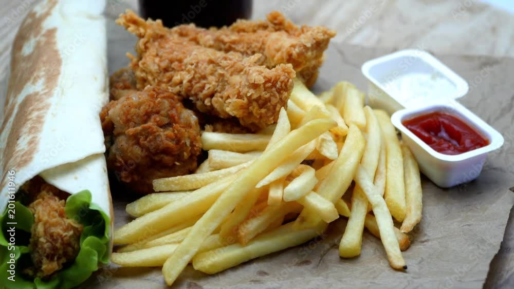 Chicken roll, french fries and chicken fries with cola. On a wooden table rotation. 4K. Chicken roll, french fries and chicken fries with cola. On a wooden table rotation. 4K.