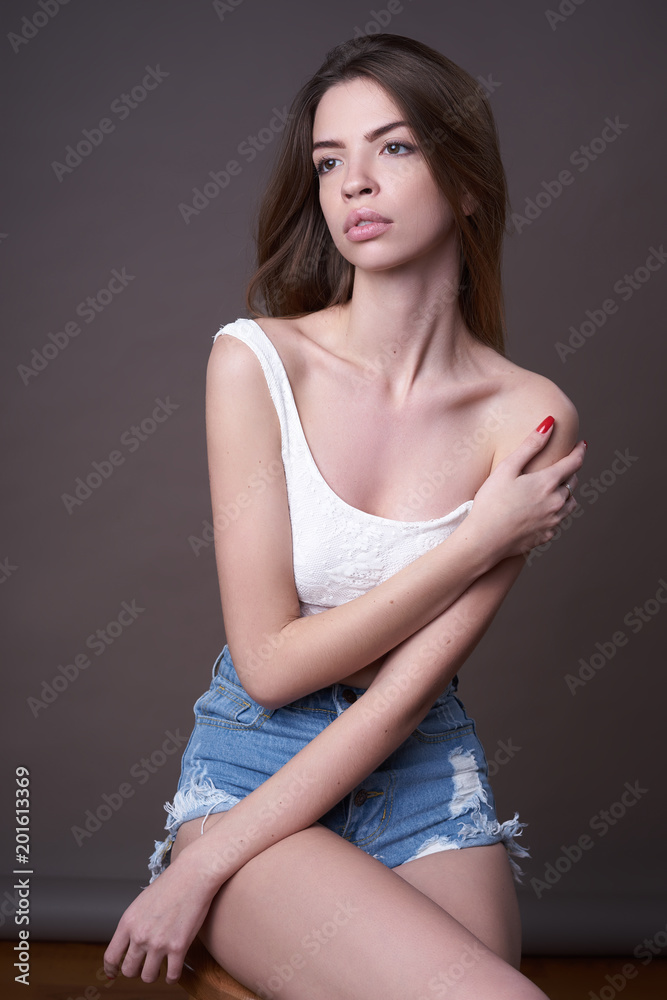 Concept: professional fashion lifestyle. Beautiful model posing in studio during classic test shooting wearing denim shorts and white lingerie. Woman show poses and emotions.