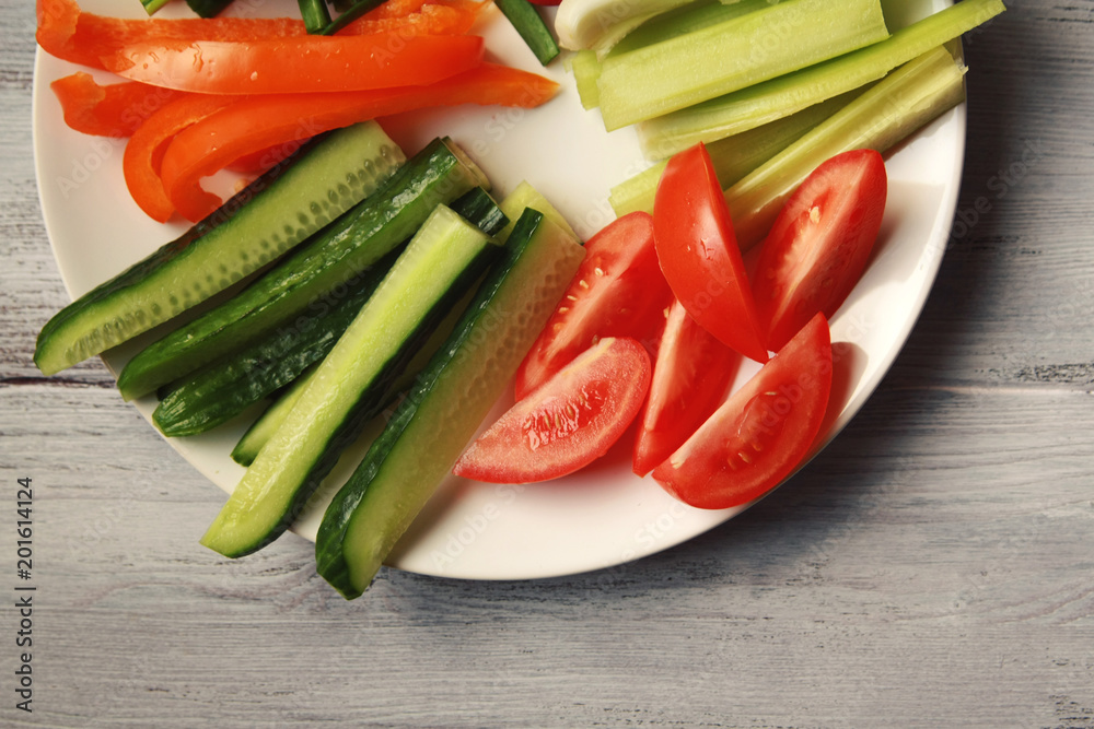 White plate with vegetables for a vegetarian salad. Radishes, tomatoes, celery, bell pepper, onion and cucumber. White wooden kitchen table. Close up. Top view. White plate with vegetables for a vegetarian salad. Radishes, tomatoes, celery, bell pepper, onion and cucumber. White wooden kitchen table. Close up. Top view.