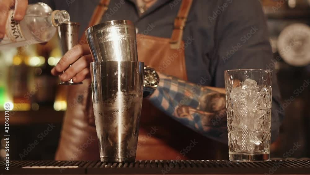 close up shot of the bartender's hands, a man pours vodka into a measuring glass, and then pours aalcohol in a nearby standing on the bar rack shaker close up shot of the bartender's hands, a man pours vodka into a measuring glass, and then pours aalcohol in a nearby standing on the bar rack shaker