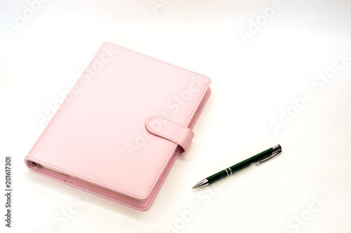 pink notebook with a ballpoint pen lying on white background
