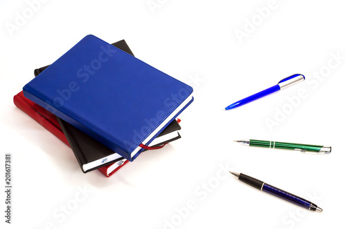 notebook lying next to ballpoint pens on white background
