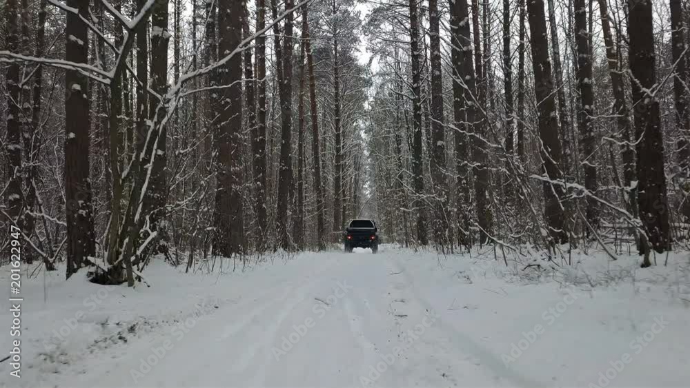 SUV 6x6 rides by winter road in snow-covered forest, back view SUV 6x6 rides by winter road in snow-covered forest, back view