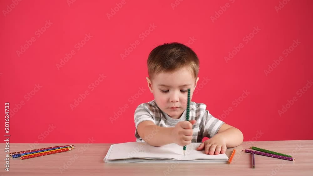 Happy child drawing with pencils in album, isolated on pink. Happy child drawing with pencils in album, isolated on pink.