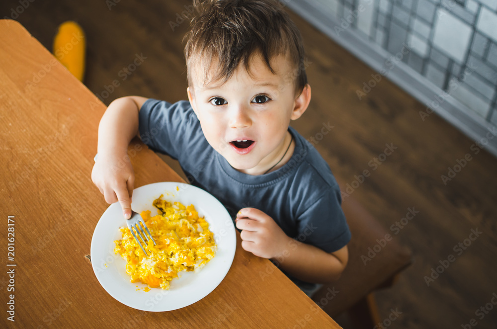 a child in a t-shirt in the kitchen eating an omelet, a fork