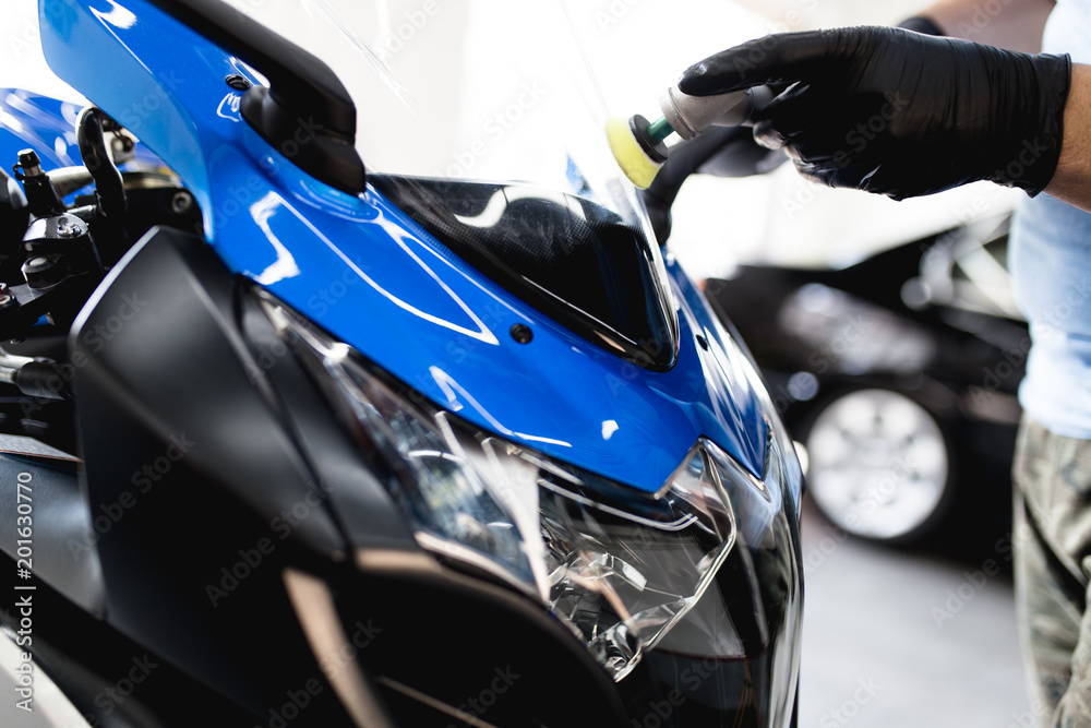 Fototapeta premium Motorcycle detailing - Man with orbital polisher in repair shop polishing motorcycle. Selective focus.