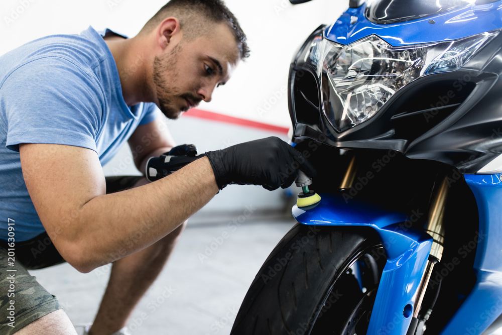 Fototapeta premium Detale motocyklowe - Człowiek z polerką orbitalną w warsztacie naprawczym motocykl. Selektywne skupienie.