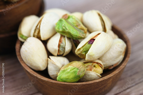 Closeup of pistachios with and without shell in wooden bowl
