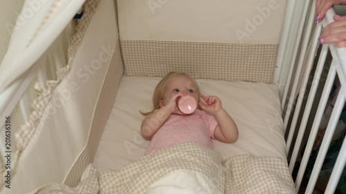 The child falls asleep in the crib. Baby is eating from a bottle in a baby cot. photo